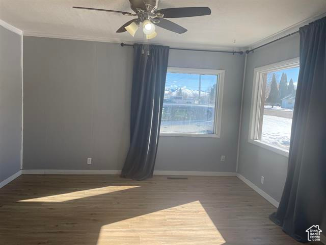Spare room with a ceiling fan, crown molding, baseboards, and wood finished floors