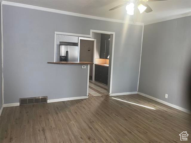 Unfurnished room with ceiling fan, dark wood-type flooring, visible vents, baseboards, and crown molding