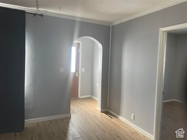 Unfurnished room with arched walkways, crown molding, wood finished floors, and baseboards