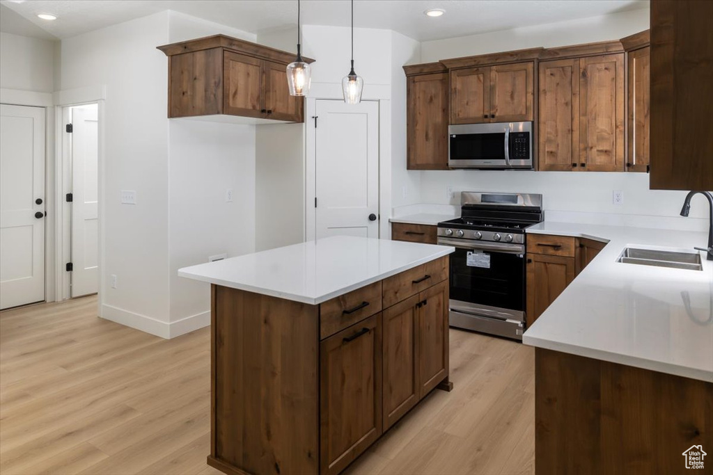 Kitchen with appliances with stainless steel finishes, light countertops, light wood-style floors, pendant lighting, and a sink