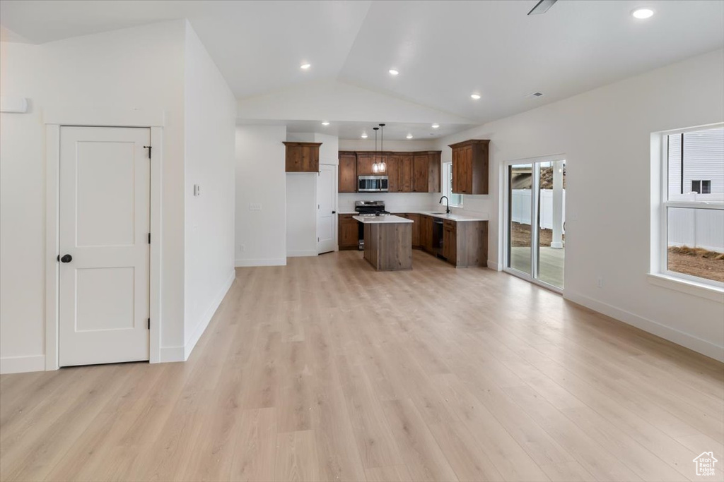 Kitchen with light wood-style flooring, open floor plan, light countertops, a center island, and stainless steel microwave