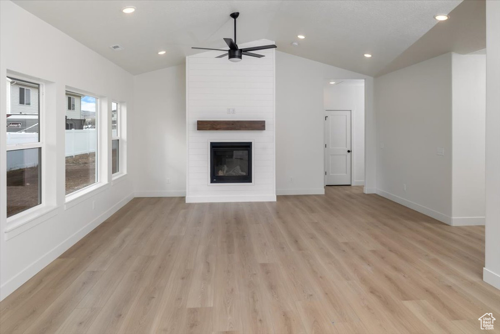 Unfurnished living room featuring lofted ceiling, a large fireplace, light wood-type flooring, and baseboards