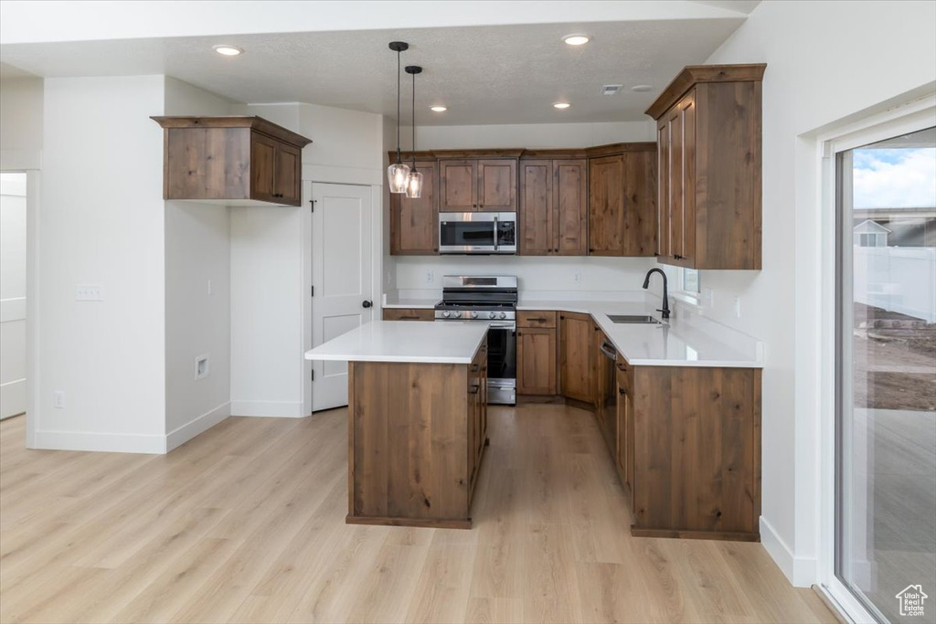 Kitchen with baseboards, a kitchen island, appliances with stainless steel finishes, light wood-style floors, and recessed lighting