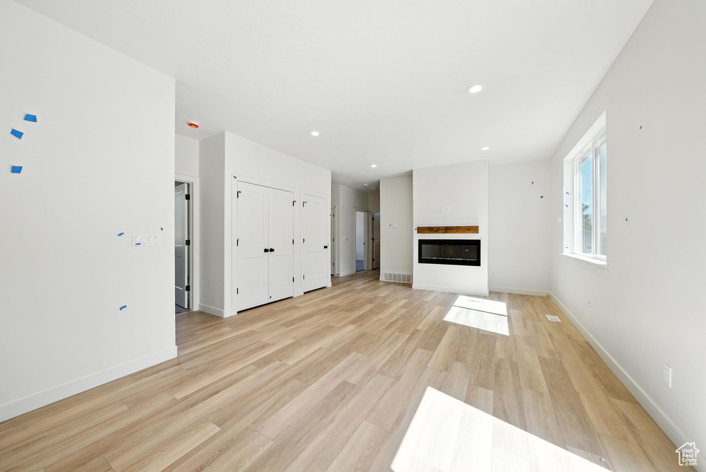 Unfurnished living room featuring a glass covered fireplace, light wood finished floors, and recessed lighting