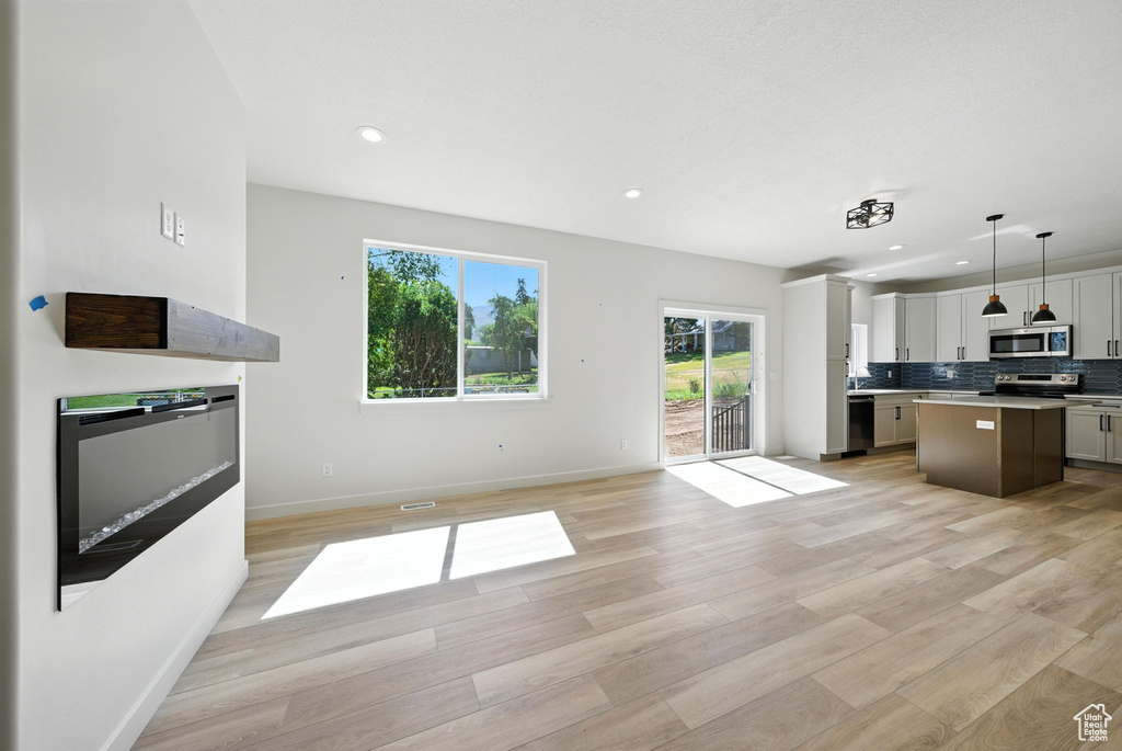 Kitchen with appliances with stainless steel finishes, open floor plan, a center island, tasteful backsplash, and light wood-type flooring