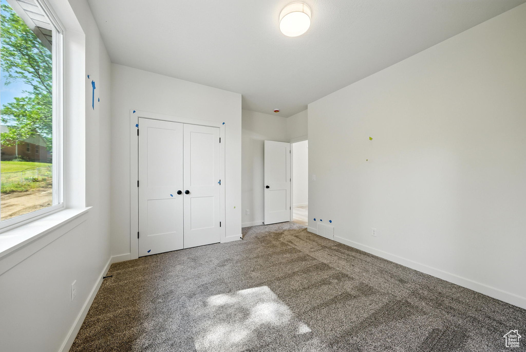 Unfurnished bedroom featuring carpet floors, multiple windows, and a closet