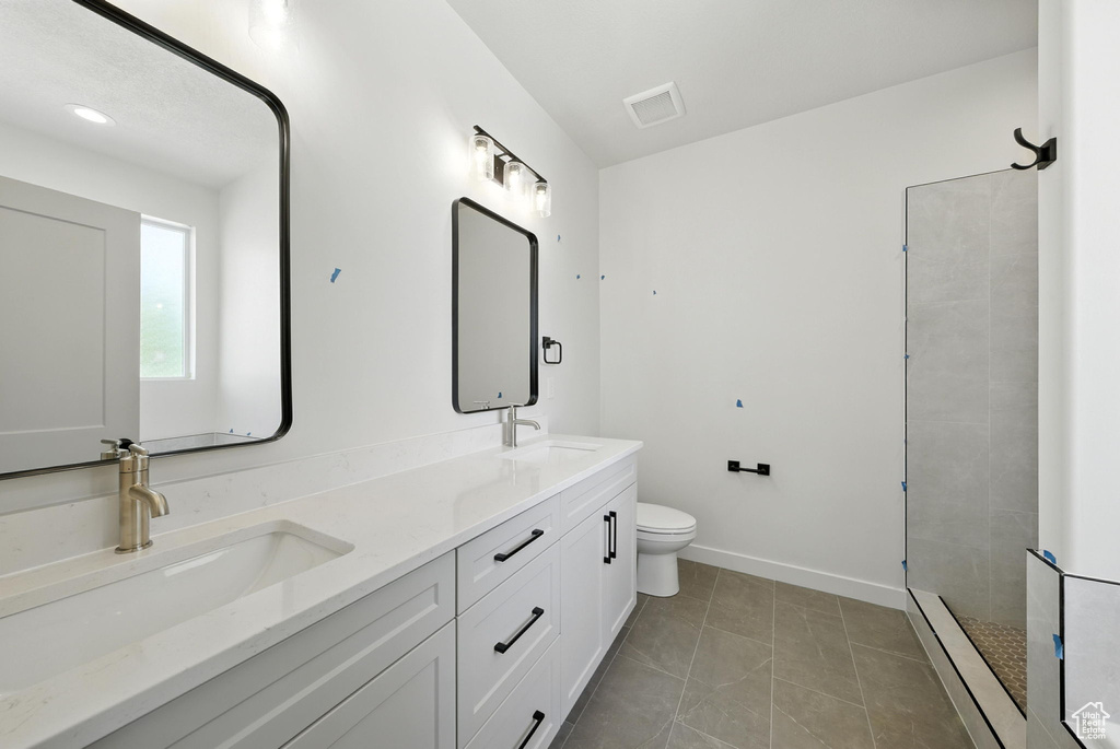 Bathroom with double vanity, a baseboard heating unit, tiled shower, and tile patterned flooring