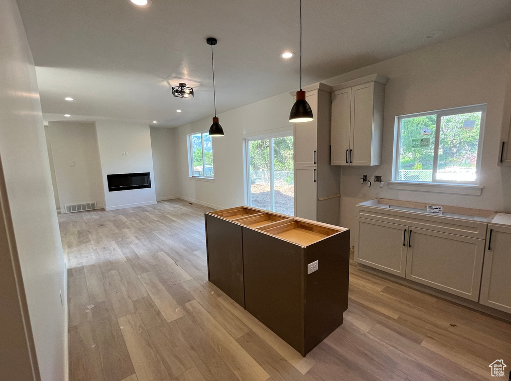 Kitchen featuring recessed lighting, light wood-style floors, pendant lighting, a center island, and a glass covered fireplace