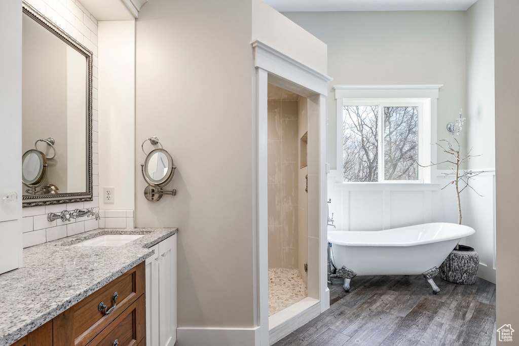 Bathroom with wood finished floors, a soaking tub, vanity, a tile shower, and backsplash