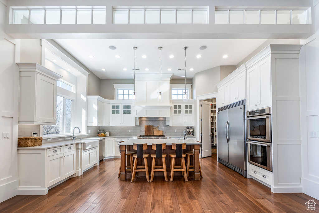 Kitchen with appliances with stainless steel finishes, dark wood-type flooring, a breakfast bar area, glass insert cabinets, and recessed lighting