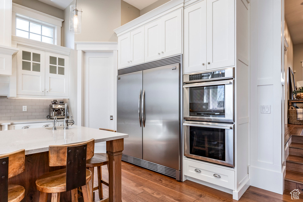 Kitchen featuring appliances with stainless steel finishes, white cabinets, decorative backsplash, a kitchen bar, and wood finished floors