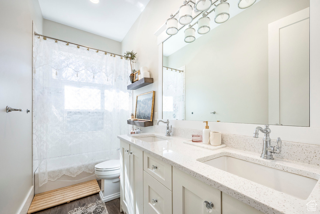 Full bath with toilet, double vanity, shower / bath combo with shower curtain, and wood finished floors