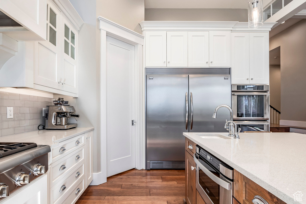 Kitchen with appliances with stainless steel finishes, a sink, dark wood-style floors, glass insert cabinets, and tasteful backsplash