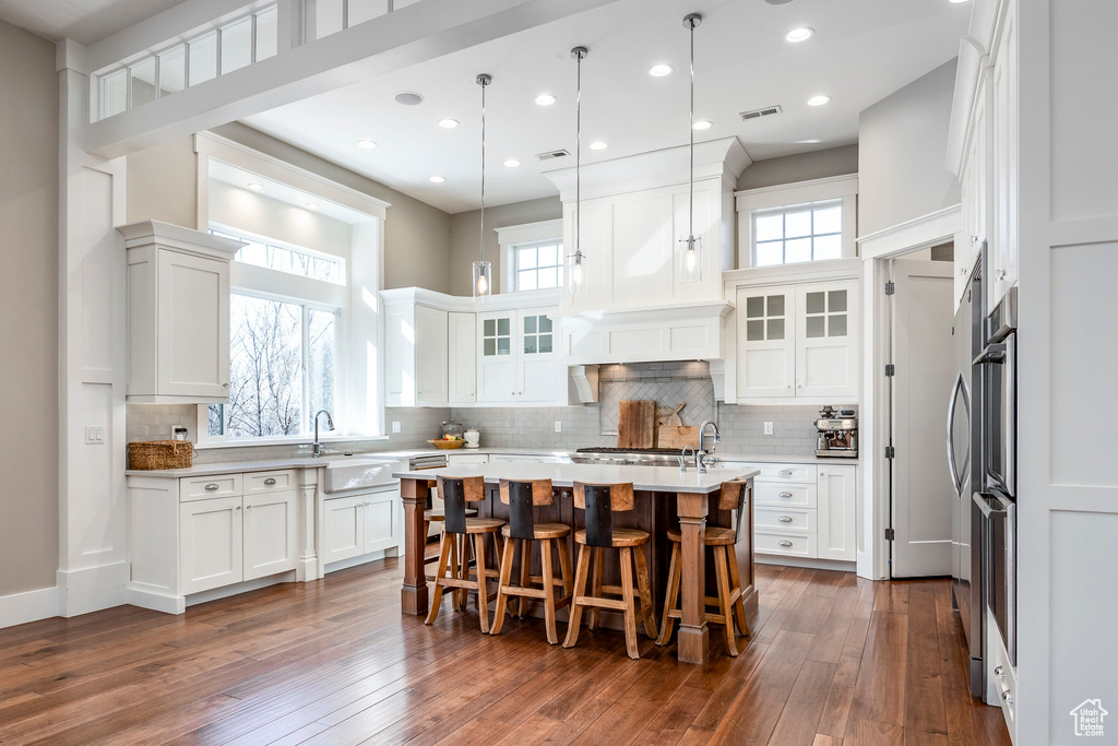 Kitchen with a sink, a kitchen island with sink, light countertops, white cabinets, and a kitchen breakfast bar