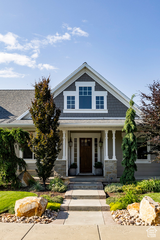 Craftsman-style house featuring a porch, a shingled roof, and stone siding