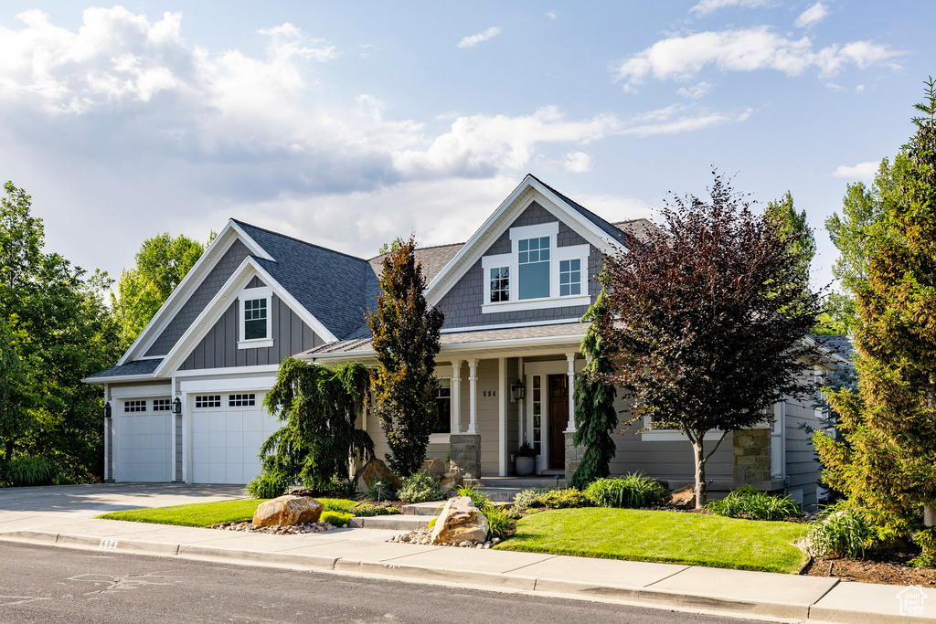 Craftsman house featuring driveway, a porch, board and batten siding, roof with shingles, and a front lawn