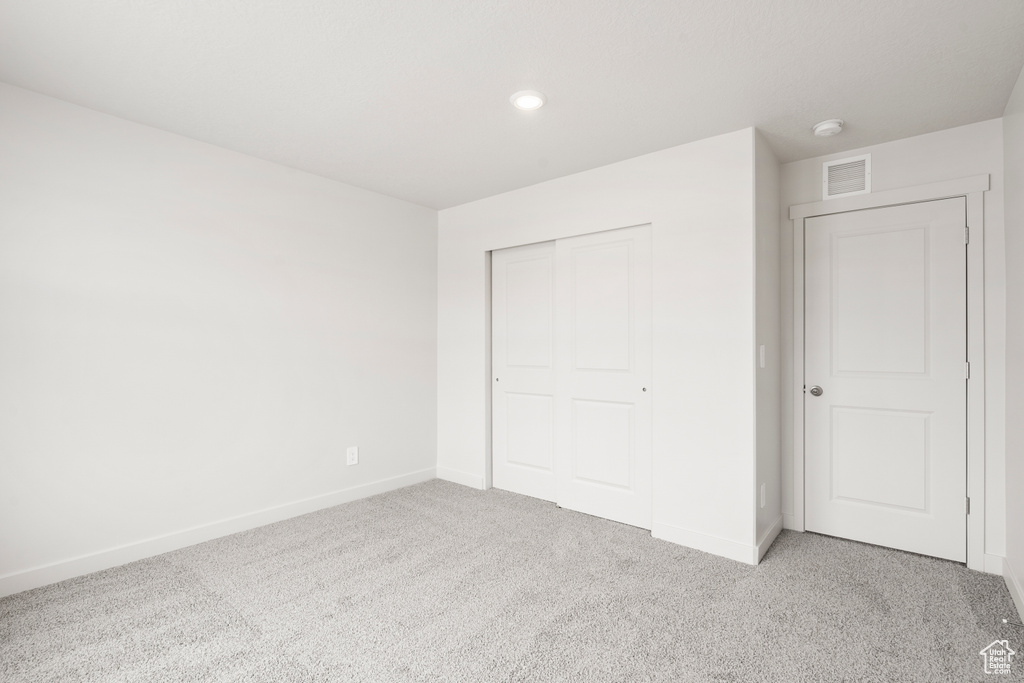 Unfurnished bedroom featuring a closet, baseboards, visible vents, and light colored carpet