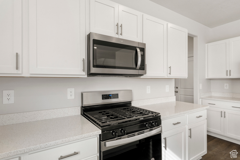 Kitchen featuring dark wood-type flooring, white cabinets, light stone countertops, and appliances with stainless steel finishes