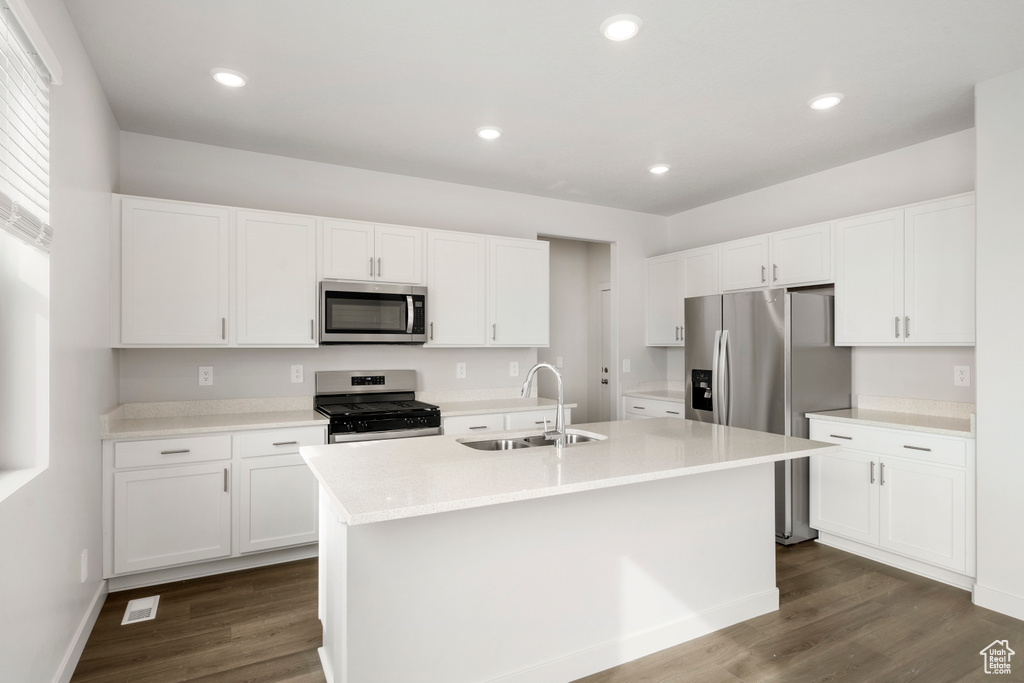 Kitchen featuring dark wood-type flooring, a sink, white cabinets, a kitchen island with sink, and appliances with stainless steel finishes