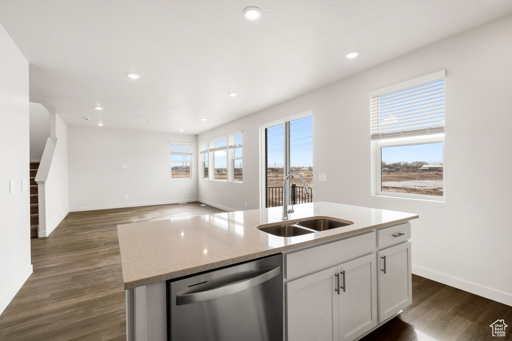 Kitchen with dark wood finished floors, stainless steel dishwasher, a sink, an island with sink, and white cabinets