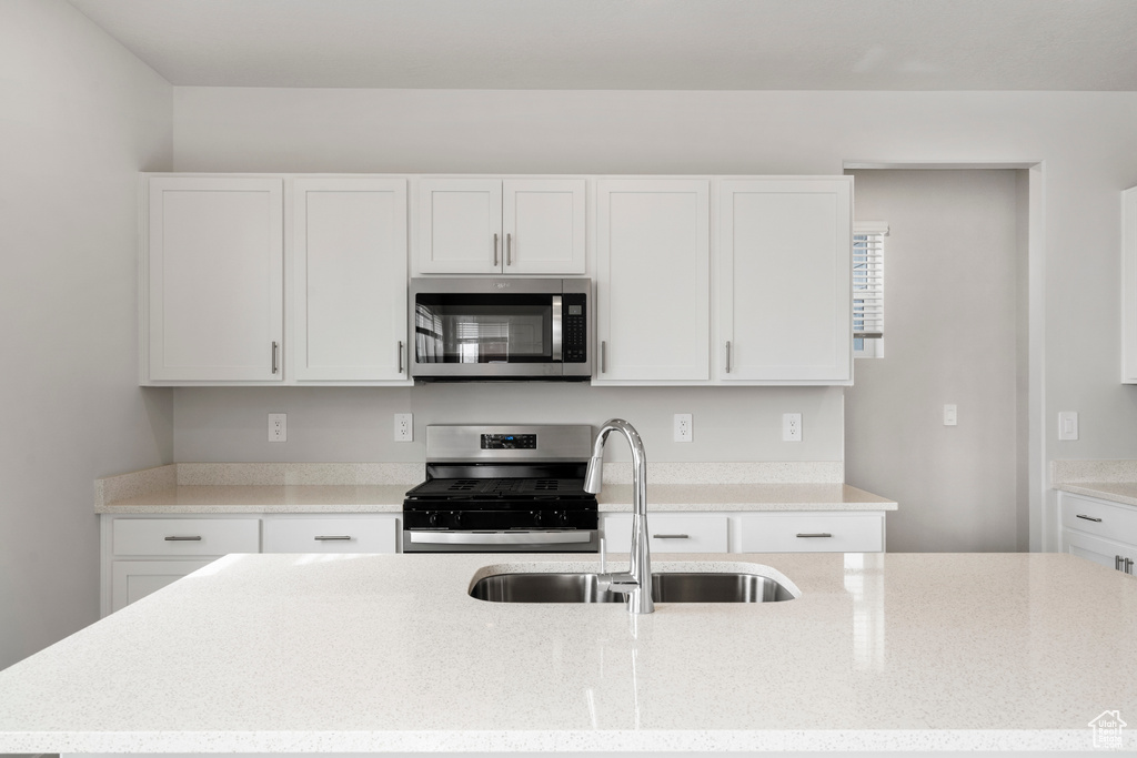 Kitchen featuring an island with sink, light stone counters, a sink, stainless steel appliances, and white cabinets