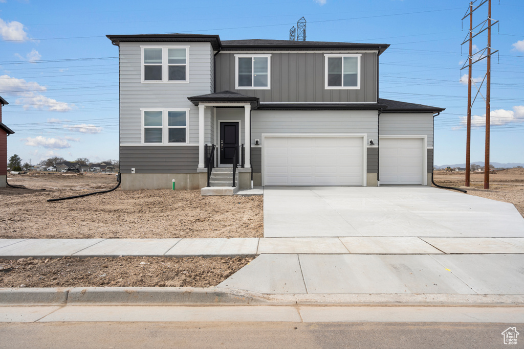 View of front facade featuring board and batten siding, driveway, and an attached garage
