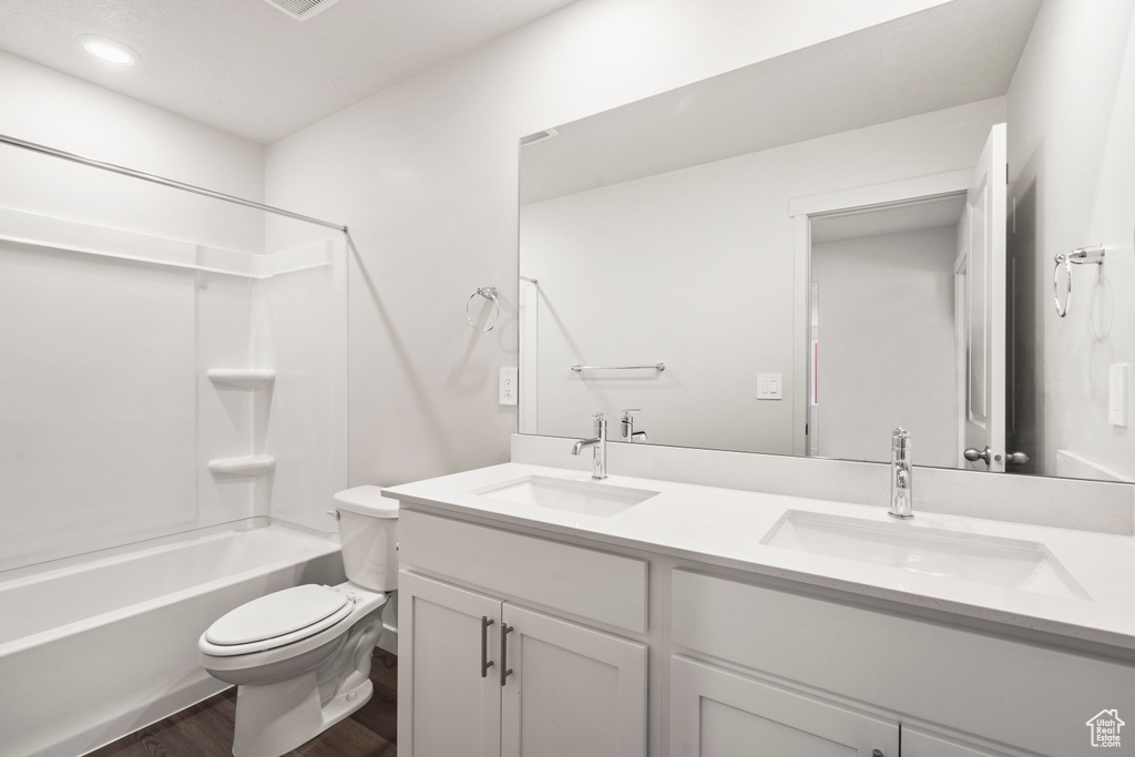 Full bath featuring double vanity, a sink, toilet, and wood finished floors