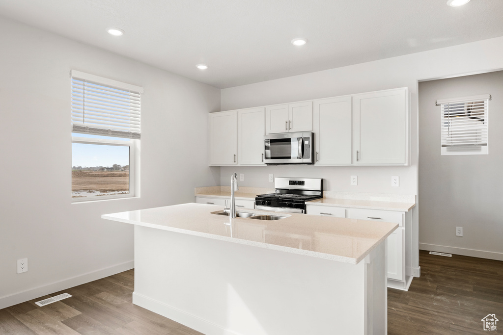 Kitchen with a sink, appliances with stainless steel finishes, an island with sink, and baseboards