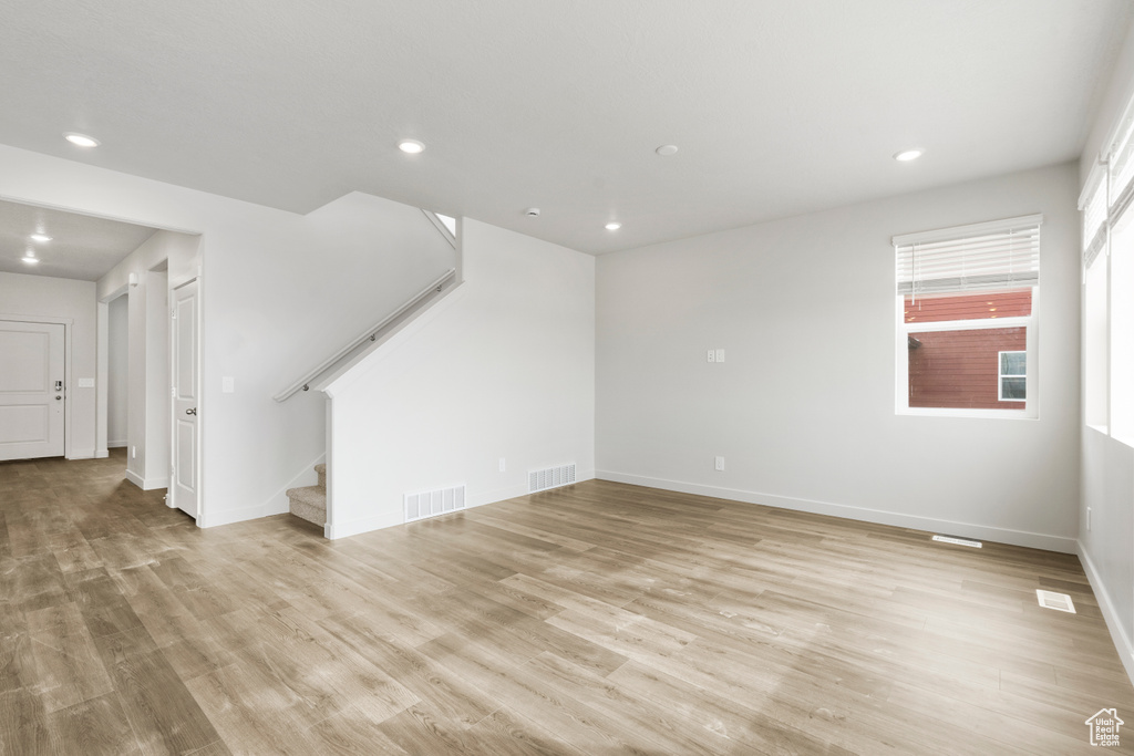 Unfurnished living room with light wood finished floors, visible vents, and stairway