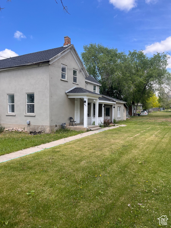 View of front of home with a chimney, covered porch, stucco siding, a front lawn, and a shingled roof