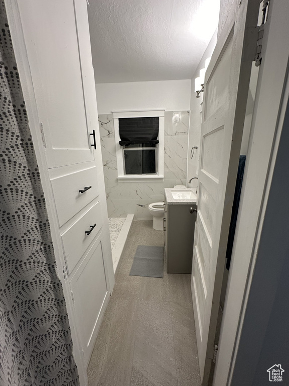 Full bath with a marble finish shower, a textured ceiling, toilet, and vanity