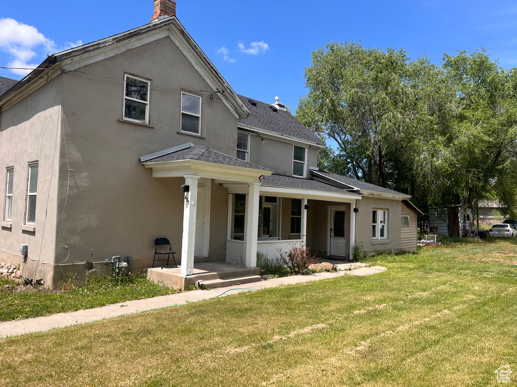 View of front of home featuring a shingled roof, a front lawn, stucco siding, a chimney, and covered porch