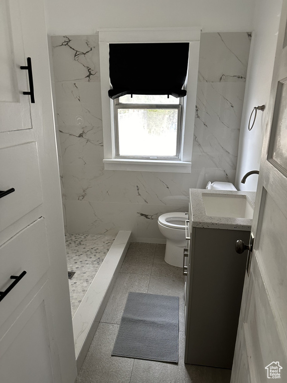 Bathroom featuring toilet, a marble finish shower, vanity, and tile walls