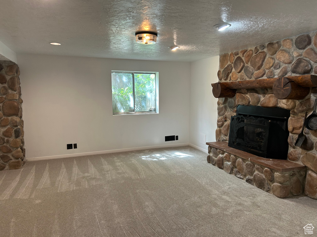 Living room with carpet, a stone fireplace, a textured ceiling, and baseboards
