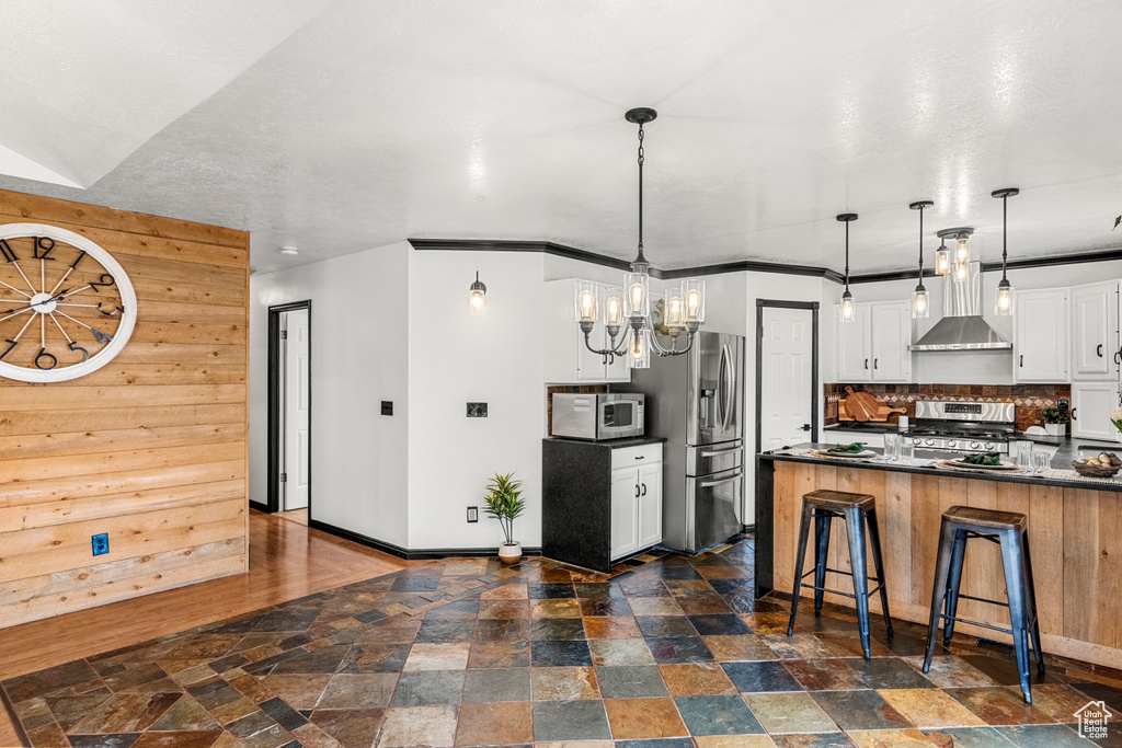 Kitchen with appliances with stainless steel finishes, dark countertops, stone finish flooring, and wall chimney range hood
