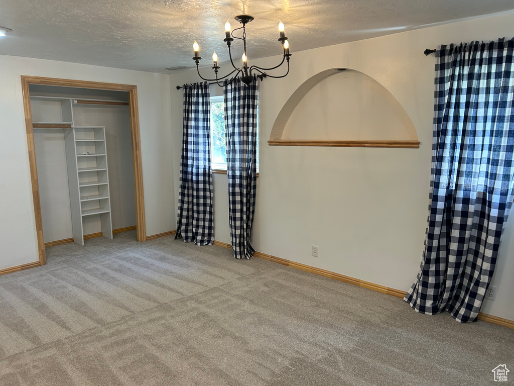 Unfurnished bedroom with a chandelier, a textured ceiling, carpet flooring, baseboards, and a closet