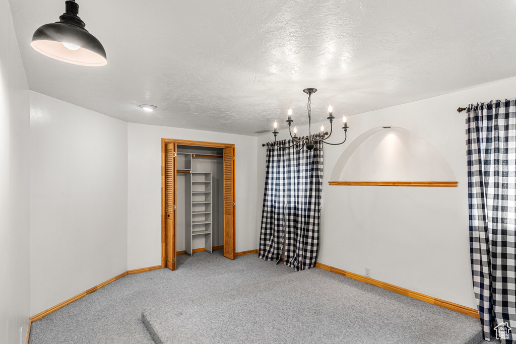 Carpeted empty room featuring a chandelier, a textured ceiling, and baseboards