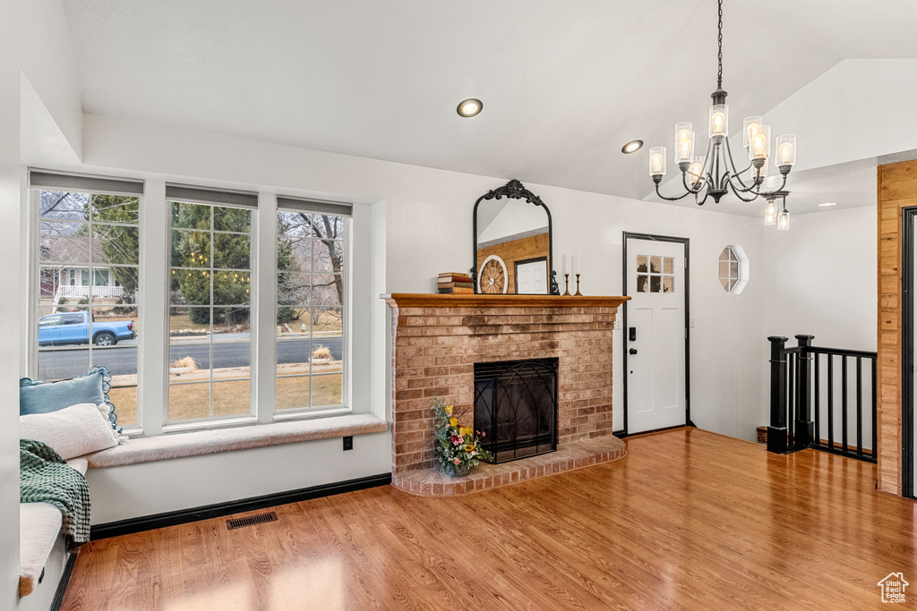Living area with lofted ceiling, visible vents, a brick fireplace, wood finished floors, and a chandelier