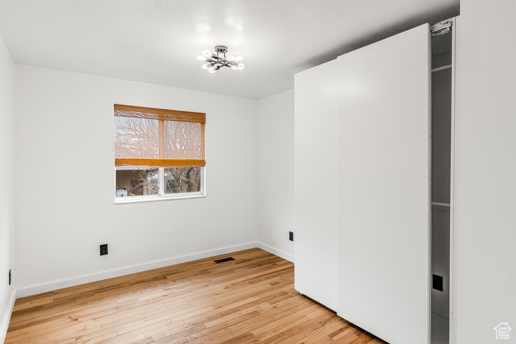 Unfurnished room with a notable chandelier, light wood finished floors, visible vents, and baseboards