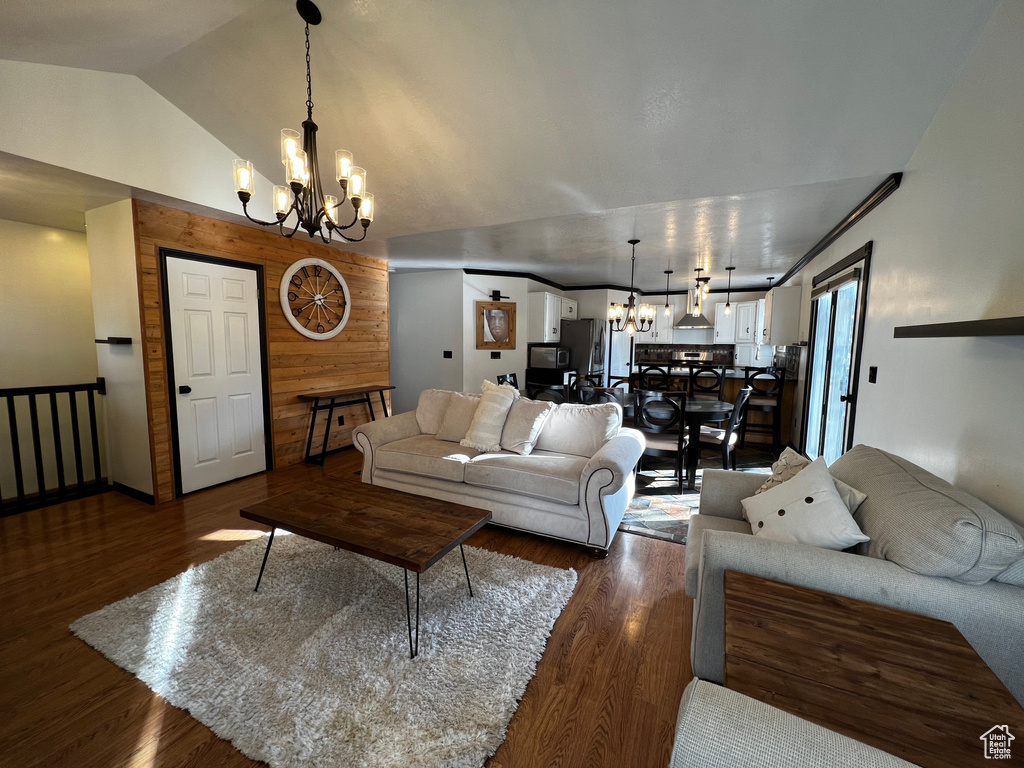 Living room with dark wood-style floors, wooden walls, vaulted ceiling, and a notable chandelier