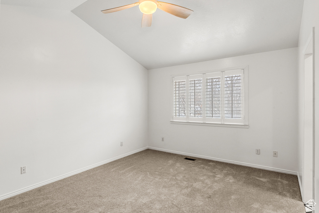 Empty room with carpet, visible vents, vaulted ceiling, ceiling fan, and baseboards