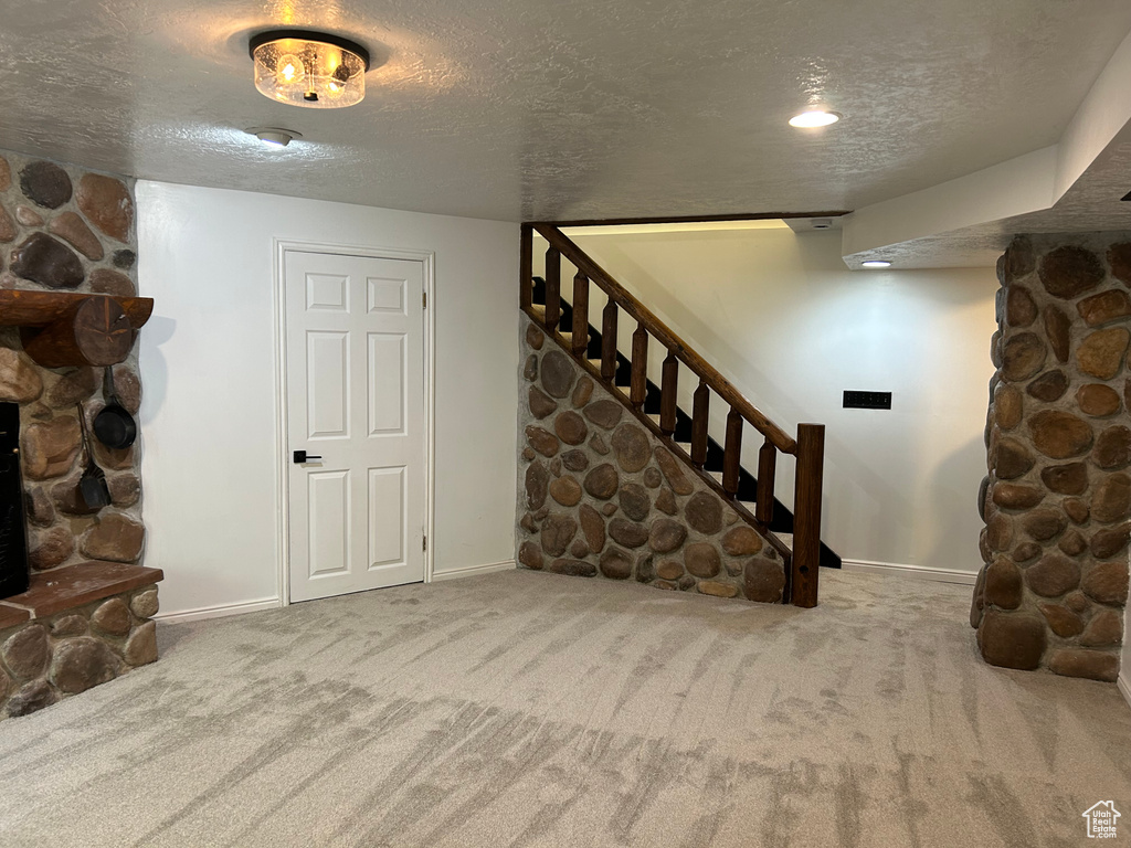 Finished basement with a textured ceiling, carpet flooring, baseboards, and stairway