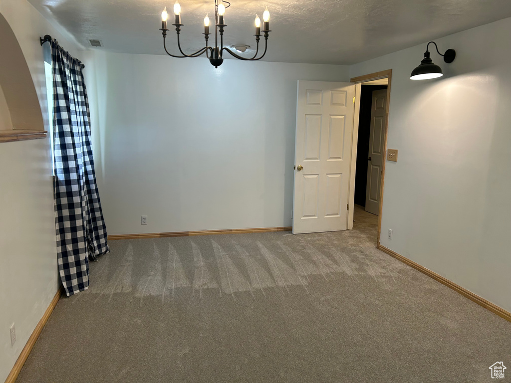 Carpeted empty room featuring a chandelier and baseboards