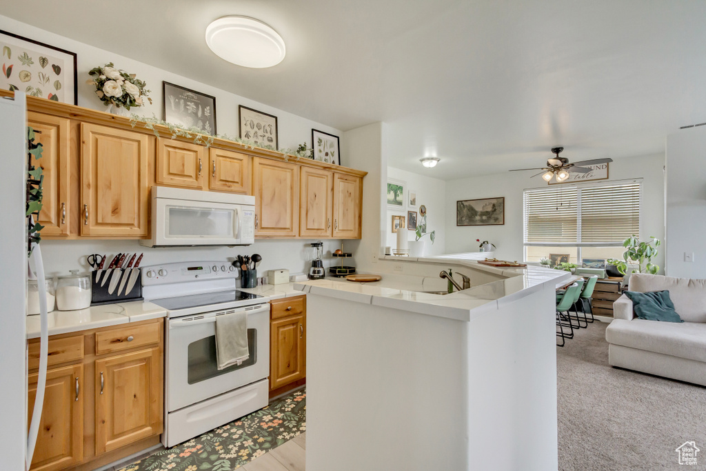 Kitchen with light brown cabinets, white appliances, a sink, open floor plan, and light countertops