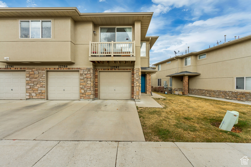 View of property featuring stucco siding, a balcony, a garage, stone siding, and driveway