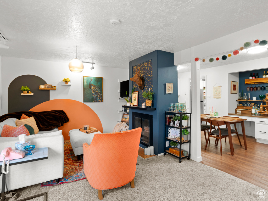 Living room with carpet floors, a fireplace with flush hearth, wood finished floors, a textured ceiling, and a bar