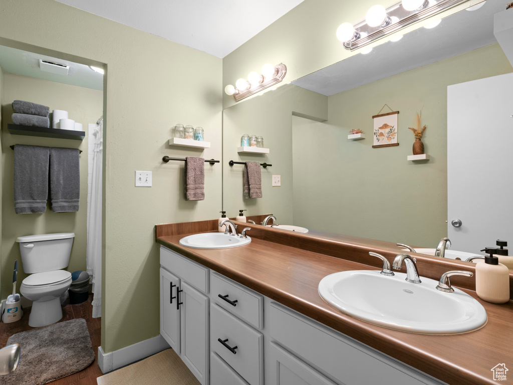 Bathroom featuring double vanity, a sink, toilet, and baseboards