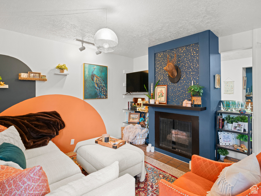 Living room with tile patterned flooring, rail lighting, a fireplace, and a textured ceiling