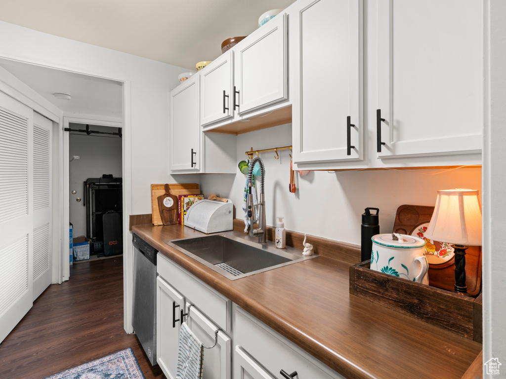 Kitchen featuring dark wood-style flooring, dark countertops, stainless steel dishwasher, white cabinetry, and a sink