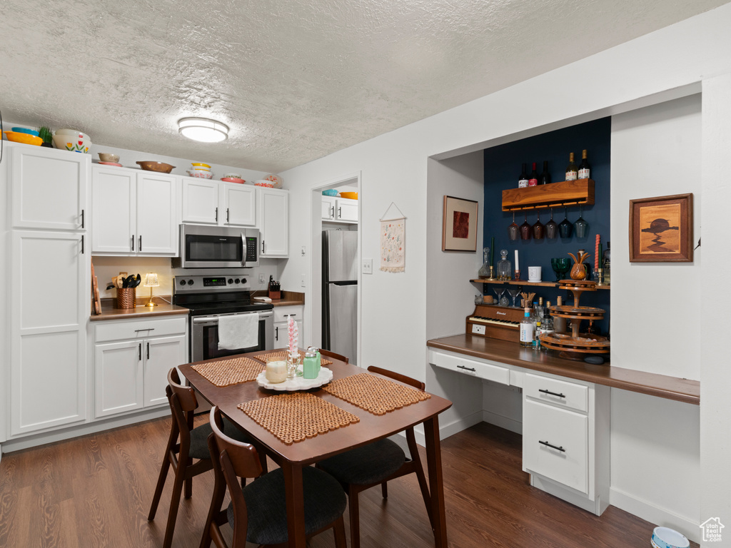 Kitchen featuring a textured ceiling, stainless steel appliances, baseboards, white cabinets, and dark wood-style floors